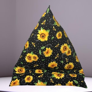 May include: A black triangular pillow with a sunflower and bee pattern. The pillow has white polka dots and a green border.
