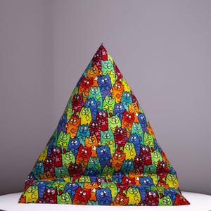 May include: A colorful beanbag chair with a vibrant pattern of cartoon cats in various colors. The beanbag has a triangular shape and sits on a white surface. The cats are in shades of red, blue, green, yellow, and orange.
