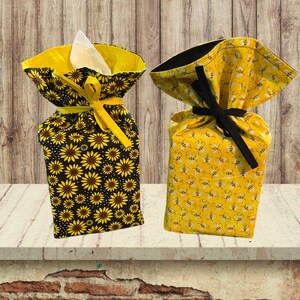 May include: Two fabric tissue box covers. One is black with yellow sunflowers and the other is yellow with black bees. Both have black ribbon ties.