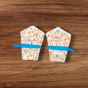 May include: A pair of white oven mitts with a blue trim and a colorful floral pattern featuring birds, flowers, and apples. The text on the mitts reads "curry's veggies" and "flowers".