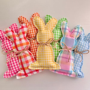 May include: Six colorful gingham bunny shaped stuffed toys. The bunnies are in shades of pink, orange, yellow, green, light blue, and blue.