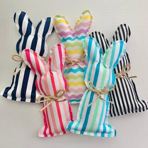 May include: Five striped fabric bunny rabbits in different colors, including blue, pink, yellow, and black. The bunnies are made of soft fabric and have a sewn-on face.