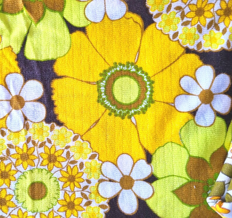 May include: A fabric with a retro floral pattern in shades of yellow, green, brown, and white. The fabric features large and small flowers with a repeating pattern.