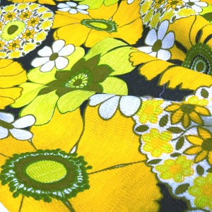 May include: Yellow fabric with a floral pattern. The flowers are white, green, and yellow. The fabric has a textured surface.