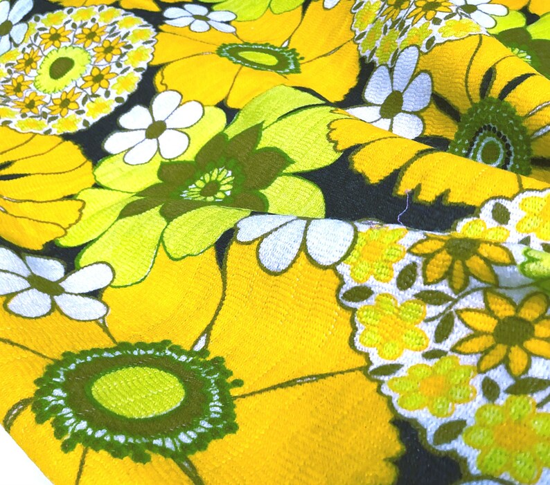 May include: Yellow fabric with a floral pattern. The flowers are white, green, and yellow. The fabric has a textured surface.
