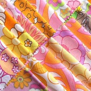 May include: A collection of fabric swatches arranged in a fan pattern, featuring various floral and geometric prints in vibrant shades of orange, yellow, pink, and white. The fabric pieces have pinked edges and display repeating patterns of stylized flowers.