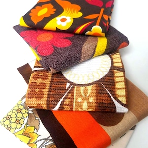 May include: A stack of four folded fabric squares featuring distinct patterns. The top piece has a dark brown background with orange and yellow floral motifs. Below it is a textured brown fabric with red flowers, followed by a brown and white geometric print, and a bottom piece with yellow floral patterns and orange stripes.