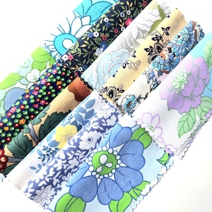 May include: A collection of fabric swatches featuring various floral patterns in shades of blue, green, yellow, and black. The strips of material are arranged diagonally, showcasing diverse botanical prints, including small blossoms and large petals.