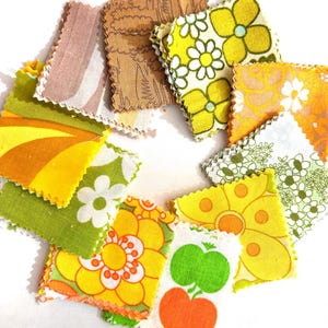 May include: A collection of square fabric swatches with pinked edges, featuring various patterns including yellow and white flowers, green floral prints, brown wood grain textures, and orange and green apple motifs arranged in a circular pattern.