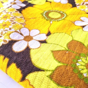 May include: A brown fabric with a yellow, green, and white floral pattern. The fabric features a variety of flower shapes and sizes, including daisies and larger, more intricate blooms.
