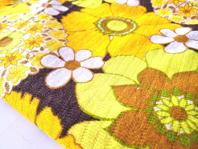 May include: A brown fabric with a yellow, green, and white floral pattern. The fabric features a variety of flower shapes and sizes, including daisies and larger, more intricate blooms.