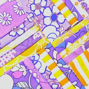 May include: A collection of fabric strips featuring a variety of patterns in shades of purple, yellow, and white. The designs include large floral motifs, small daisy prints, geometric shapes, and bold yellow and white stripes with pinked edges.