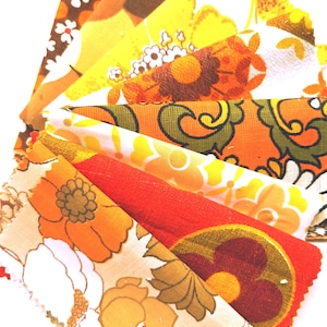 May include: A collection of fabric swatches arranged in a fan shape, featuring various floral patterns in vibrant shades of orange, yellow, brown, and white. Each piece of textile displays distinct botanical motifs with scalloped or pinked edges.