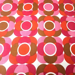May include: A repeating pattern of large, stylized flowers in shades of pink, red, orange, and brown on a white background. Each flower has a white circle in the centre. The design is reminiscent of vintage textiles.