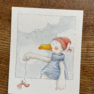 Könnte beinhalten: Aquarellillustration einer Cartoon-Möwe mit blauem Pullover und roter Strickmütze mit Bommel. Die Möwe fischt mit einem Wurm an einer Leine. Der Hintergrund zeigt einen bewölkten Himmel.