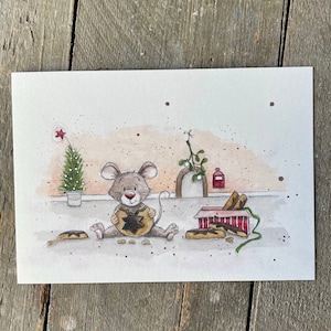Könnte beinhalten: Eine Aquarell-Illustration einer niedlichen Maus, die ein sternförmiges Keks hält. Die Maus sitzt auf einer hellbraunen Oberfläche mit einem kleinen Weihnachtsbaum und einer Schachtel Kekse im Hintergrund.