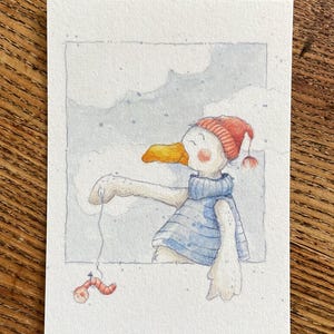 Könnte beinhalten: Aquarellillustration einer Cartoon-Gans mit roter Strickmütze und blauem Pullover, die mit einem Wurm angelt. Die Gans hat einen gelben Schnabel und ist vor einem bewölkten, hellblauen Hintergrund dargestellt.