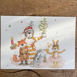 Könnte beinhalten: Eine Aquarellillustration einer Gruppe von Waldtieren, die Weihnachten feiern. Ein Bär mit einem gestreiften Hut und Pyjama hält einen kleinen Weihnachtsbaum. Ein Fuchs mit einem roten Schal hält ein Schwein, das einen braunen Pullover trägt. Ein Dachs hält eine Laterne und ein Kaninchen mit einem rosa Tutu hält einen Stern.
