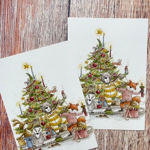 Könnte beinhalten: Eine Aquarellillustration einer Gruppe von Waldtieren, die Weihnachten um einen geschmückten Weihnachtsbaum feiern. Zu den Tieren gehören ein Bär, ein Fuchs, ein Kaninchen, ein Dachs und ein Eichhörnchen. Der Bär trägt einen gelb-weiß gestreiften Pullover und der Fuchs einen rosa Pullover. Die Tiere halten Geschenke und Dekorationen in den Händen. Der Weihnachtsbaum ist mit roten und goldenen Kugeln, einem Stern obenauf und einem roten Band geschmückt.