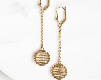 May include: Gold dangle earrings with a geometric circle design. The earrings have a delicate chain and a simple hook closure.