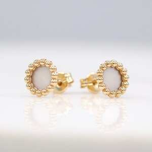 Puede incluir: Un par de pendientes de oro con un centro circular blanco rodeado por un anillo de pequeñas cuentas doradas.