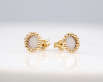 May include: A pair of gold earrings with a white circular center surrounded by a ring of small gold beads.