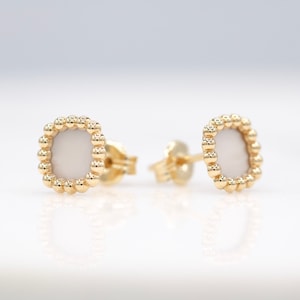 Puede incluir: Un par de pendientes de oro con una piedra blanca cuadrada engastada en un marco de cuentas.