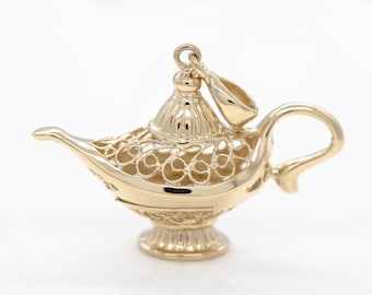 May include: A gold-colored genie lamp charm with an intricate filigree design. The lamp has a lid with a finial and a loop for hanging.