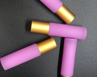 May include: Four lavender-colored roller bottles with gold caps. The bottles are arranged in a triangular shape on a black surface.