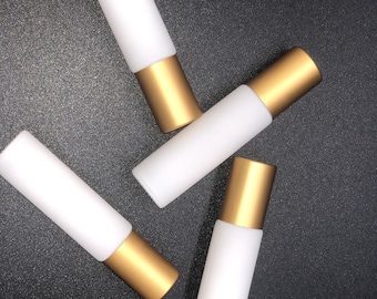 May include: Four white glass roller bottles with gold caps. The bottles are arranged in a scattered pattern on a black surface.