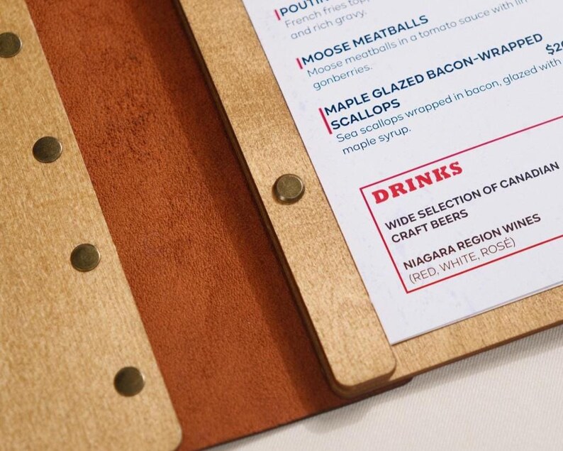Natural plywood cover open on a table, interior pages with "Drinks" section visible. Leather spine on the right edge. This is a drinks menu specific shot — same plywood format as the food menu but showing the drinks section. Useful for buyers planning matching covers for food and drinks menus. Having the same plywood cover format across both menus creates a consistent table presentation — a detail that communicates care and professionalism in the dining room without being expensive to achieve.