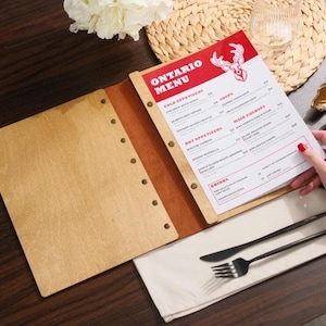 Natural plywood cover open on a table, interior pages with "Drinks" section visible. Leather spine on the right edge. This is a drinks menu specific shot — same plywood format as the food menu but showing the drinks section. Useful for buyers planning matching covers for food and drinks menus. Having the same plywood cover format across both menus creates a consistent table presentation — a detail that communicates care and professionalism in the dining room without being expensive to achieve.