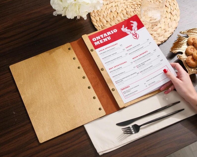 Natural plywood cover open on a table, interior pages with "Drinks" section visible. Leather spine on the right edge. This is a drinks menu specific shot — same plywood format as the food menu but showing the drinks section. Useful for buyers planning matching covers for food and drinks menus. Having the same plywood cover format across both menus creates a consistent table presentation — a detail that communicates care and professionalism in the dining room without being expensive to achieve.
