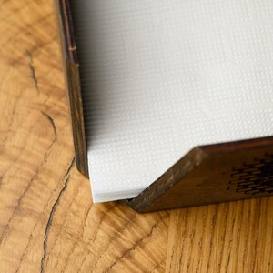 Side view of a dark walnut-stained plywood angled napkin holder with white paper napkins on a white clean surface. The open angled top, dark finish, and clean construction are shown from the side profile. Handcrafted custom engraved wooden napkin holder for pub table service, restaurant dining, bar counters, and hospitality interior styling with personalized laser engraving and plywood stain color options on Etsy marketplace.