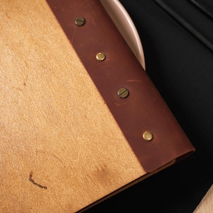 Natural plywood cover open on a table, interior pages with "Drinks" section visible. Leather spine on the right edge. This is a drinks menu specific shot — same plywood format as the food menu but showing the drinks section. Useful for buyers planning matching covers for food and drinks menus. Having the same plywood cover format across both menus creates a consistent table presentation — a detail that communicates care and professionalism in the dining room without being expensive to achieve.