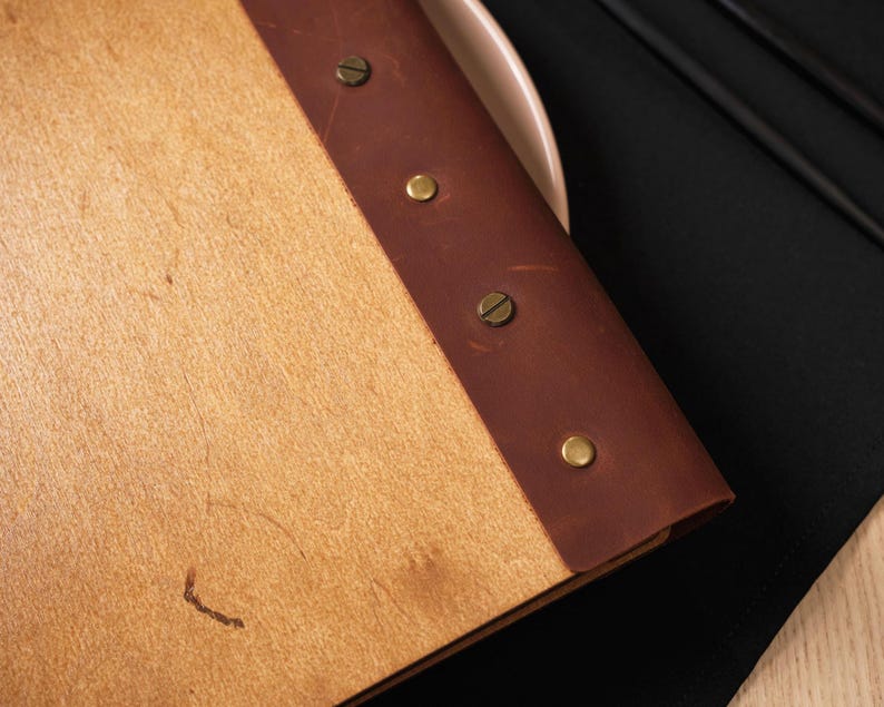 Natural plywood cover open on a table, interior pages with "Drinks" section visible. Leather spine on the right edge. This is a drinks menu specific shot — same plywood format as the food menu but showing the drinks section. Useful for buyers planning matching covers for food and drinks menus. Having the same plywood cover format across both menus creates a consistent table presentation — a detail that communicates care and professionalism in the dining room without being expensive to achieve.