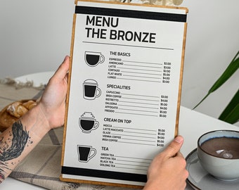May include: A menu titled "THE BRONZE" with a wooden frame, displaying coffee and tea options. The menu includes prices for espresso, latte, cappuccino, and more. The menu is held by a person.