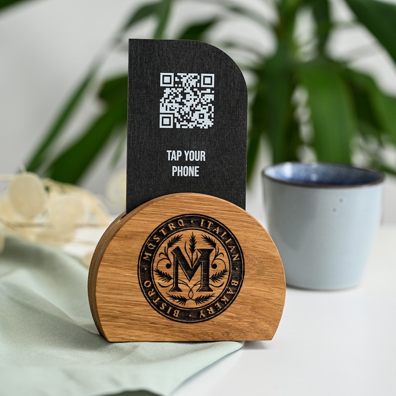 Maestro
Front view of a custom NFC menu stand showing the black display panel with Spotify logo, Tap Your Phone and NFC contactless symbol alongside the natural oak semicircle base with the detailed laser engraved Maestro Italian restaurant circular badge logo. The premium black and oak design and branded NFC panel make this stand a distinctive contactless digital menu solution for Italian restaurants, wine bars and upscale dining venues.
