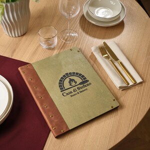 Może przedstawiać: Nakrycie stołu w restauracji z menu z napisem "Casa di Stefano Bistro & Bakery", białą miską, kieliszkiem do wina i złotymi sztućcami. Menu jest w kolorze beżowym i brązowym o skórzanej fakturze.