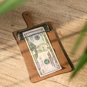 Pode incluir: Uma tábua de cortar de madeira feita à mão com um acabamento natural. A tábua apresenta uma borda viva de um lado e uma forma retangular lisa. Tem aproximadamente 45 cm de comprimento e 30 cm de largura.