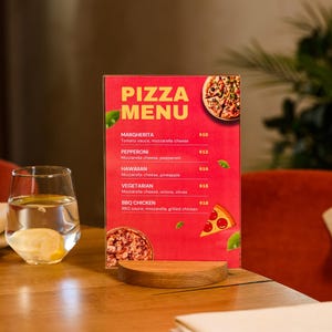 Könnte beinhalten: Eine rote Pizza-Speisekarte mit gelbem Text, die Pizza-Optionen wie Margherita, Pepperoni und Hawaiianisch auflistet. Ein Glas Wasser mit Zitrone steht auf einem Holztisch. Die Speisekarte steht auf einem Holzständer.