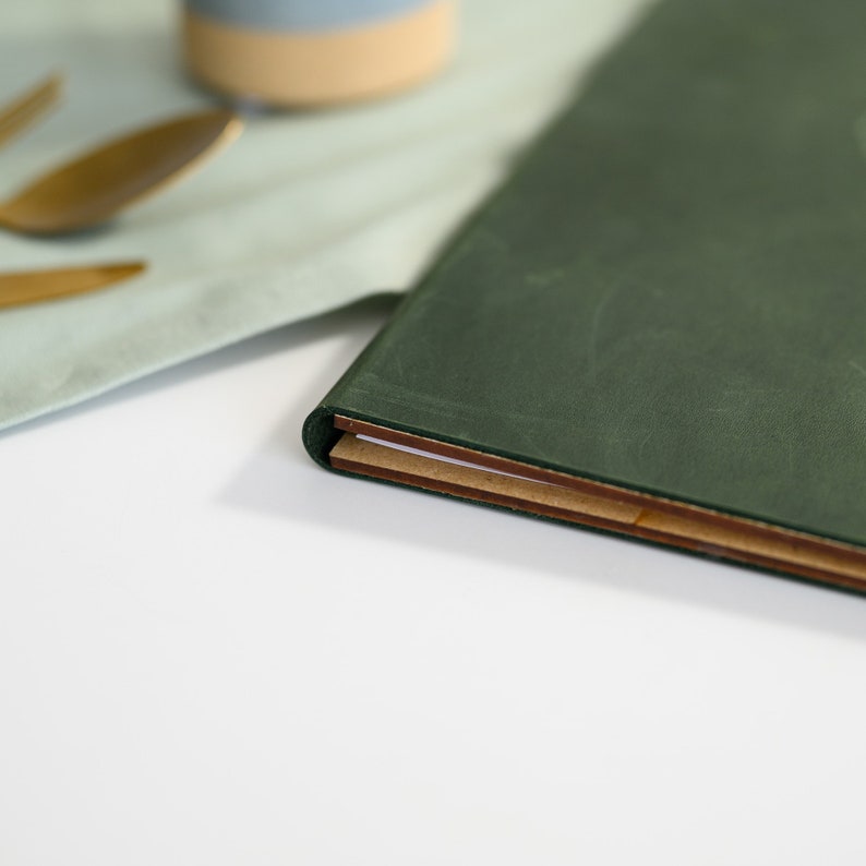 Close-up of the right edge of a dark forest green Crazy Horse leather menu cover showing the gold screw post binding hardware set into the genuine aged leather surface. The rich dark green leather with natural color variation and authentic Crazy Horse texture patina clearly visible around the hardware detail. Durable screw post binding for daily cafe and restaurant menu holder use in fine dining venues.