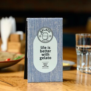 May include: A blue and white menu with the text "Gelato" in a circle with a small ice cream cone graphic. The text "life is better with gelato" is below the circle. The text "Sweet and Mellow" is in a circle below the text.