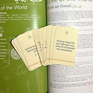 Puede incluir: Un montón de tarjetas color crema con esquinas redondeadas, con diseños florales dorados y texto. Las tarjetas están abanicadas, con una tarjeta que muestra la cita: "Lo que está destinado para ti te alcanzará, incluso si está debajo de dos montañas."