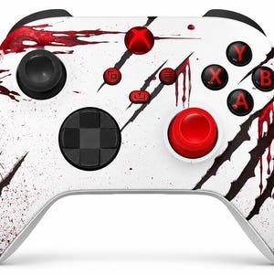 May include: A white video game controller featuring a red and black claw mark graphic pattern. The device includes a red Xbox button, red action buttons labelled A, B, X, and Y, a red right thumbstick, a black left thumbstick, and a black D-pad.