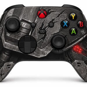 May include: A wireless video game controller featuring a dark, metallic, battle-worn aesthetic with a cracked surface design. It includes a glowing red Xbox button, black analogue sticks, a directional pad, and standard coloured Y, X, B, and A buttons.