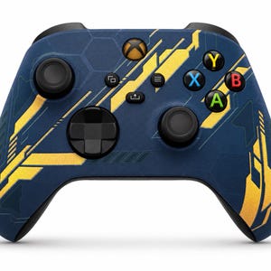 May include: A wireless video game controller featuring a dark blue base with a hexagonal pattern and bright yellow geometric accents. The device includes black analogue sticks, a directional pad, and standard action buttons labelled Y, X, B, and A.