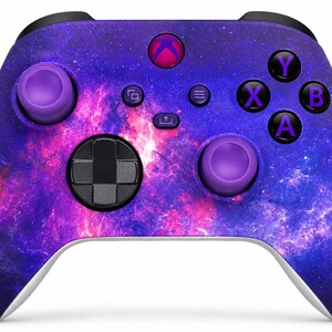 May include: A wireless video game controller featuring a vibrant galaxy print in shades of deep blue, purple, and bright pink. The device includes two purple thumbsticks, a black directional pad, and black action buttons labelled A, B, X, and Y.