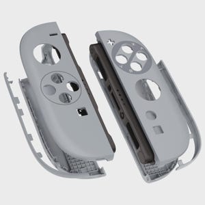 May include: Two gray game controller shells, disassembled, revealing internal components. The shells have button cutouts and are designed to fit a handheld gaming device. The design includes a directional pad, action buttons, and other control features.