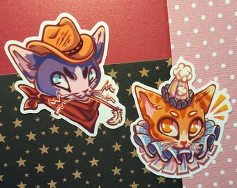 May include: Two cat stickers. One is a blue and purple cat wearing a cowboy hat and red bandana, holding a piece of straw. The other is an orange cat wearing a party hat and ruffled collar.